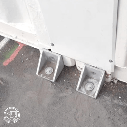 Shipping container bolt down brackets securing container to ground, made from durable steel with twist lock design.
