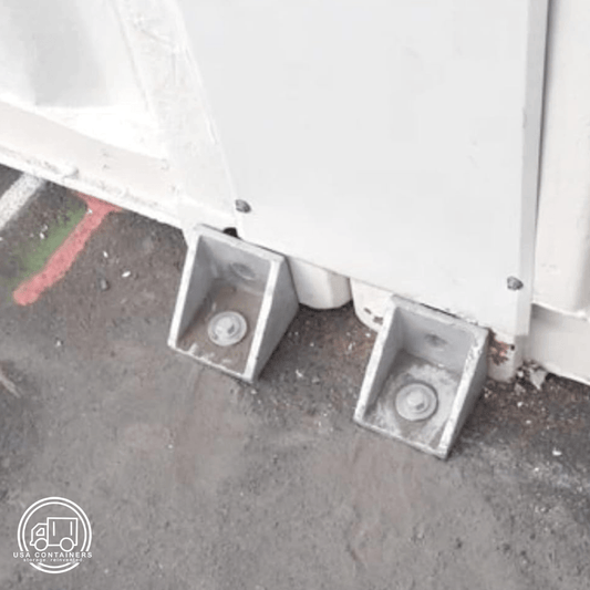 Shipping container bolt down brackets securing container to ground, made from durable steel with twist lock design.