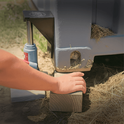 Close-up of a hand placing a wooden block under a shipping container lifted by a bracket and 6-ton bottle jack bundle.